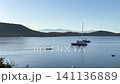 A wide, peaceful view of a calm blue bay featuring anchored luxury yachts, a rowing team in a scull boat, and scenic rolling hills beneath a clear morning sky. High quality 4k footage 141136889