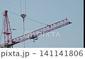A tall crane stands at a construction site, lifting materials into the air. 141141806