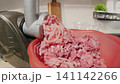 Closeup of meat grinder depositing fresh beef into mixing bowl. Cozy kitchen atmosphere showing beef being minced and collected in bowl for meal preparation 141142266