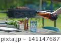 Pouring beer into glass at outdoor table during sunny day with fresh salad and grill in background 141147687