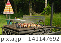 Close-up view of hand rotating meat skewers on outdoor grill over hot coals in backyard 141147692