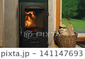 Close-up view of small log burner during evening at cozy wooden cabin. Flames rise inside wood stove heating tiny log cabin space 141147693