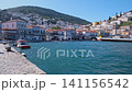 The Timeless Charm of Hydra Harbor. A picturesque view of Hydra's harbor featuring a vintage green lamp post against a backdrop of traditional white-washed houses and the sparkling Aegean Sea. 141156542