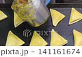 A hand uses a pastry brush to apply egg wash to triangular puff pastry turnovers before baking. 141161674