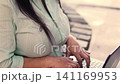 Beautiful mature Latina executive professional, with headphones and her cell phone, working on her laptop and enjoying the day, sitting in a park. Learning, home office 141169953
