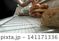 Hands pressing torn bread onto wire cooling rack beside stack of freshly baked loaves in warm kitchen light, low angle view with soft focus, rustic crust texture, cozy homemade baking atmosphere 141171336
