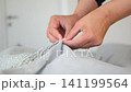 Close-Up of Hands Fixing a Fabric Sheet with Precise Attention to Detail 141199564