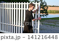 Caucasian boy closes heavy automatic gate of modern countryside house. 141216448