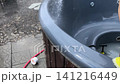 person washes large grey jacuzzi tub with water hose spray in cozy garden backyard. 141216449