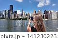 Woman photographing the new york city skyline with her phone 141230223