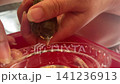Vertical close up shot of a person gently holding a tiny rescued baby sparrow bird in hands helping it to drink water from a small plastic cap indoors. 141236913