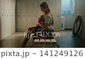 Young Gymnast Sitting Alone in Locker Room Stretching Feet with Resistance Bands 141249126