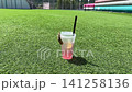 Video of a plastic cup with iced pink lemonade, a lemon slice, and a black straw, decorated with a dried citrus wheel attached by a wooden clothespin, standing on a bright green artificial turf field 141258136