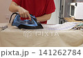 Hands iron a checked towel on a padded board in a home kitchen during a household laundry routine. 141262784