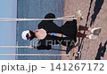 Woman in black dress swings on sandy beach, taking photos with smartphone while enjoying the view of the water and distant shoreline 141267172
