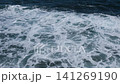 Ocean waves continuously crash against a rocky shoreline, creating foam patterns and dynamic water movement in a coastal setting 141269190