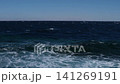 Ocean waves continuously crash onto the shoreline, illustrating the rhythmic motion of water against the sandy beach under a bright sky 141269191