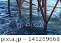 Wooden pier supports stand in ocean water, with waves gently lapping against the posts and reflections visible on the water's surface 141269668