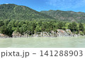Wide-angle view of the turquoise Katun river flowing past rocky cliffs and high green mountains covered with dense coniferous forest under a blue sky 141288903