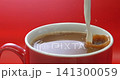 Cream pouring into black coffee in a red mug on red background, super slow motion 1000 fps 141300059
