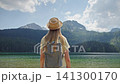 Young woman with backpack admiring the mountain landscape of Black Lake in Durmitor National Park, Montenegro. Scenic summer view of the famous glacial lake surrounded by forest and peaks 141300170