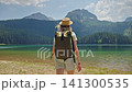 Teenage girl with backpack walking toward Black Lake in Durmitor National Park, Montenegro. Scenic summer landscape of the famous glacial lake surrounded by mountains and forest 141300535