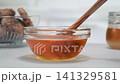 Golden honey flowing from wooden dipper into transparent glass bowl, smooth texture, bright kitchen background, advertising video, slow motion 141329581