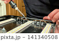 A person focuses intently on soldering wires to a circuit board while sitting at a wooden workbench, surrounded by tools and components, creating something unique 141340508