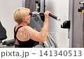 A woman does pull-ups at the gym using a resistance machine. She shows her strength and determination during the workout session 141340513