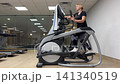 A person is using an elliptical machine in a gym. The workout involves moving arms and legs in a rhythmic manner 141340519