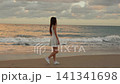 Woman walking toward ocean waves on a sandy beach at sunset 141341698