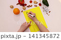 Overhead hands writing plan diet on yellow notecard surrounded by fruit nuts and measuring tape for healthy eating planning 141345872