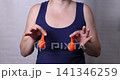 Adult woman torso in navy sleeveless top holds two orange balloons against chest while their shape deflates, creating medical concept reference with neutral gray background and soft studio lighting 141346259