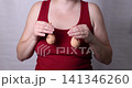 Adult female torso in red sleeveless top holding pair of breast prosthetics at chest level in centered studio view with soft light and plain gray background, with breast, health, beauty, plastic 141346260