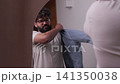 Young man with beard getting dressed in front of mirror 141350038