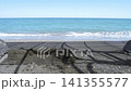 Sand is molded along the beach as waves wash ashore, with shadows from a fence creating intricate designs on the sand surface 141355577
