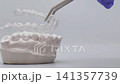 Dentist hand in blue glove removing clear aligner from plaster dental model using tweezers. Orthodontic concept with copy space 141357739