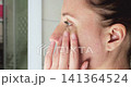 Woman gently applies moisturizing face cream during daily skincare routine. Healthy skin, facial care, natural beauty, hydration and personal wellness with an authentic self-care ritual. Close-up 141364524