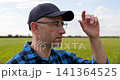 Experienced farmer looks across green wheat field while adjusting cap. Vertical video represents crop monitoring, agricultural expertise, sustainable farming and confident field management. 141364525