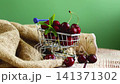Sweet red cherries in small metal shopping trolley on wooden table 141371302