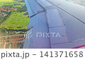 Airplane wing view during descent over green fields and urban areas, showcasing the gradual approach to landing with visible landscape and structures below 141371658