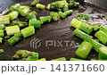 Fresh green asparagus pieces sauteing in a black frying pan, showing vibrant colors and textures as they cook in a heated kitchen environment 141371660