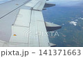 Aircraft wing with visible flaps and ailerons in flight, showcasing the landscape below with clouds and fields in the background 141371663