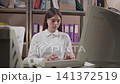 Young woman typing at office desk in storage style back office with binders, beige keyboard, desktop computer, and CRT monitor visible in tidy clerical workspace 141372519