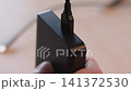 Hand steadies matte black adapter while micro usb cable seats into recessed top port, showing clean indoor technology connection with soft warm blur and tight closeup detail 141372530
