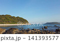 A scenic coastline with lush green hills and clear blue sky during a calm spring afternoon in April. Smooth footage captures a quiet bay with rocks in the shallow turquoise sea near Fukuoka, Japan. 141393577
