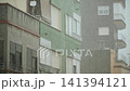 Facades of southern houses with roller shutters on windows during rain. Overcast day with heavy rainfall. Streaks and dampness on exterior walls of houses. 141394121