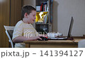 Caucasian boy smiles while playing on laptop with cast on arm in room. Online game of teen gamer and different emotions during rounds. Using computer during restrictions. 141394127