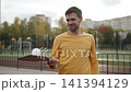 Portrait of slim man rolling perforated pickleball ball on wooden paddle. Middle aged guy bouncing plastic ball while warming up before game and training reaction. 141394129
