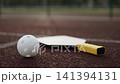 White pickleball ball rotates on sports stadium next to paddle in closeup. Sports accessories on rubberized surface of outdoor court. 141394131